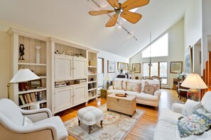 A spacious living room with a high ceiling, white furniture, and a large window providing natural light. - Hamptons Beach House (East Hampton)