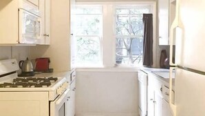 A narrow kitchen with white cabinets, a stove, and a window.