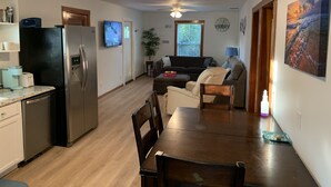 Eine kompakte Küche mit Kühlschrank, Mikrowelle und Kaffeemaschine. Ein Esstisch mit Stühlen befindet sich in der Mitte des Raumes, und eine Couch steht an der Wand.