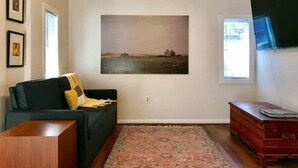 A living room with a dark sofa, a rug, a wooden cabinet, and a large landscape painting on the wall. - Montrose Place #4 Sum (Houston)