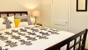 A neatly made bed with a pineapple-themed duvet, a bedside lamp, and a wooden chair. - Montrose Place #4 Sum (Houston)