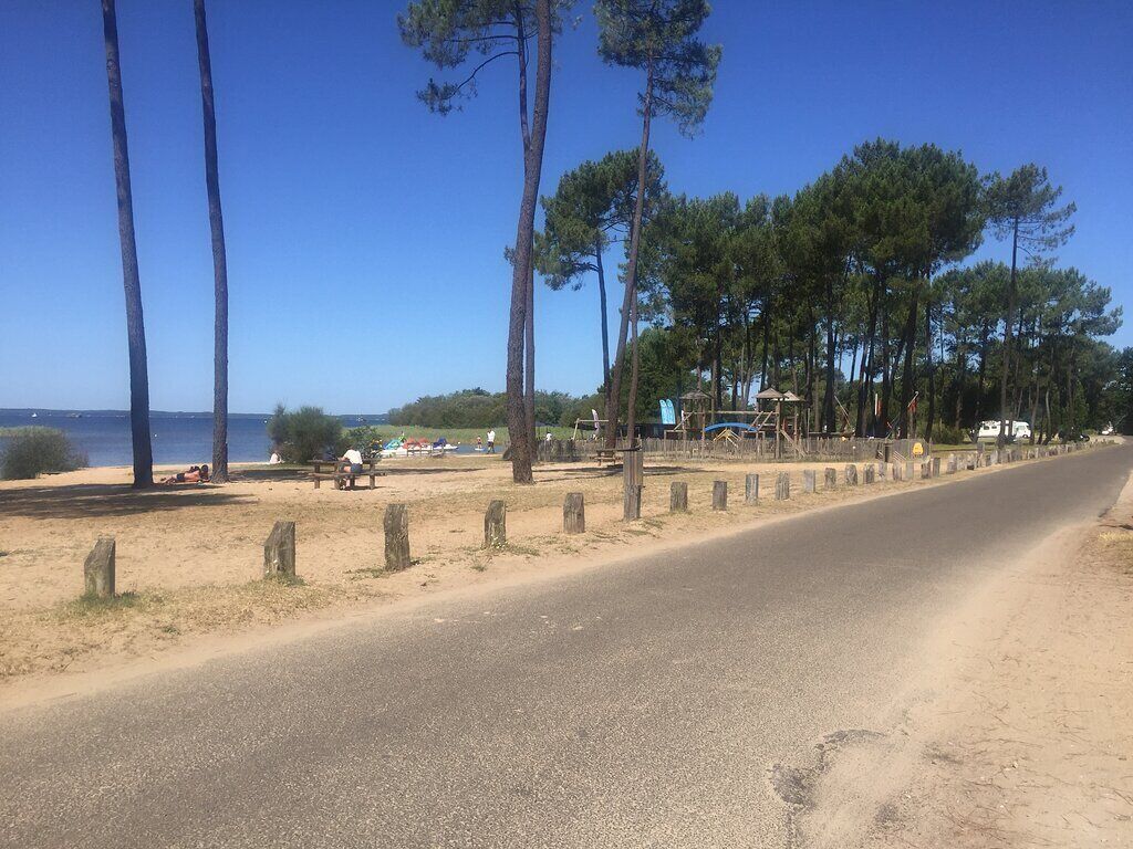 Eine Straße mit sandigem Seitenstreifen, Bäumen und einem Strand im Hintergrund.