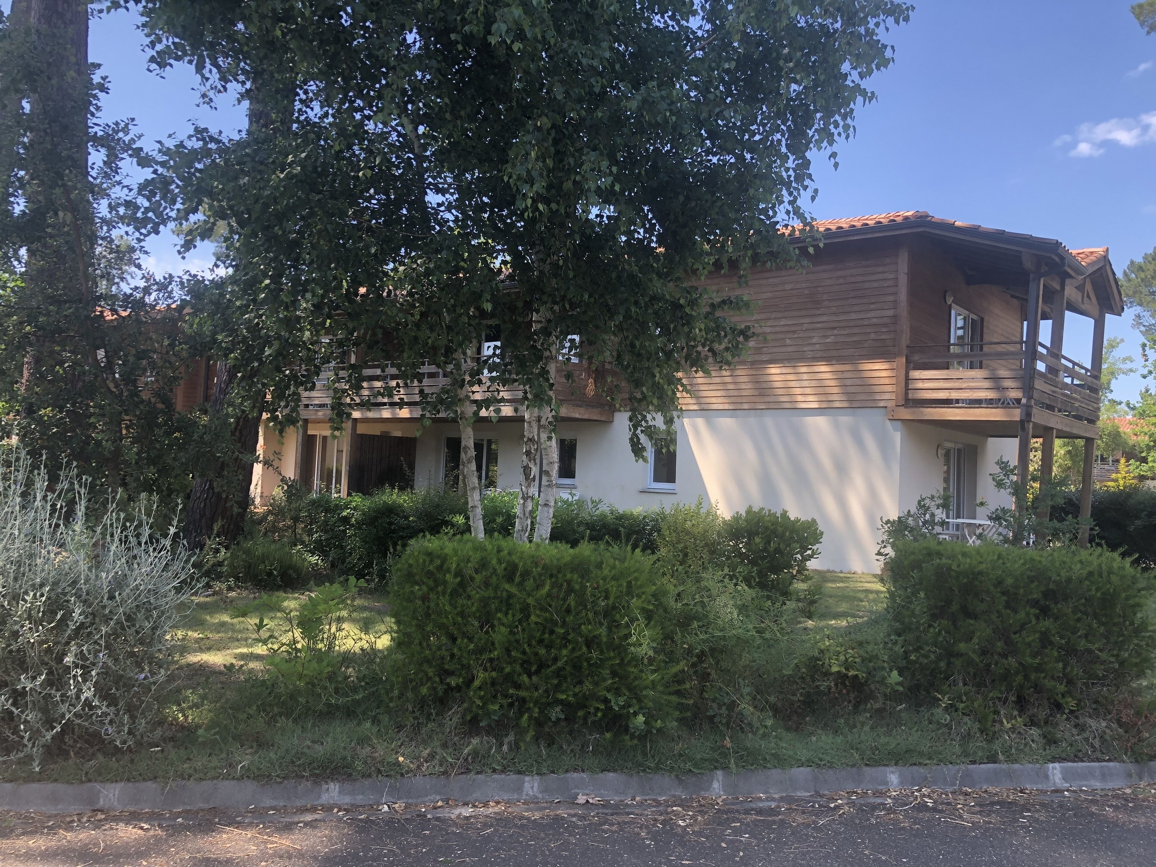 Una casa de dos pisos con balcón, rodeada de follaje y árboles.