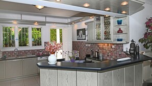 A modern kitchen with a central island, white cabinetry, and a backsplash with a mosaic pattern. - Villa Supreme (Megara)