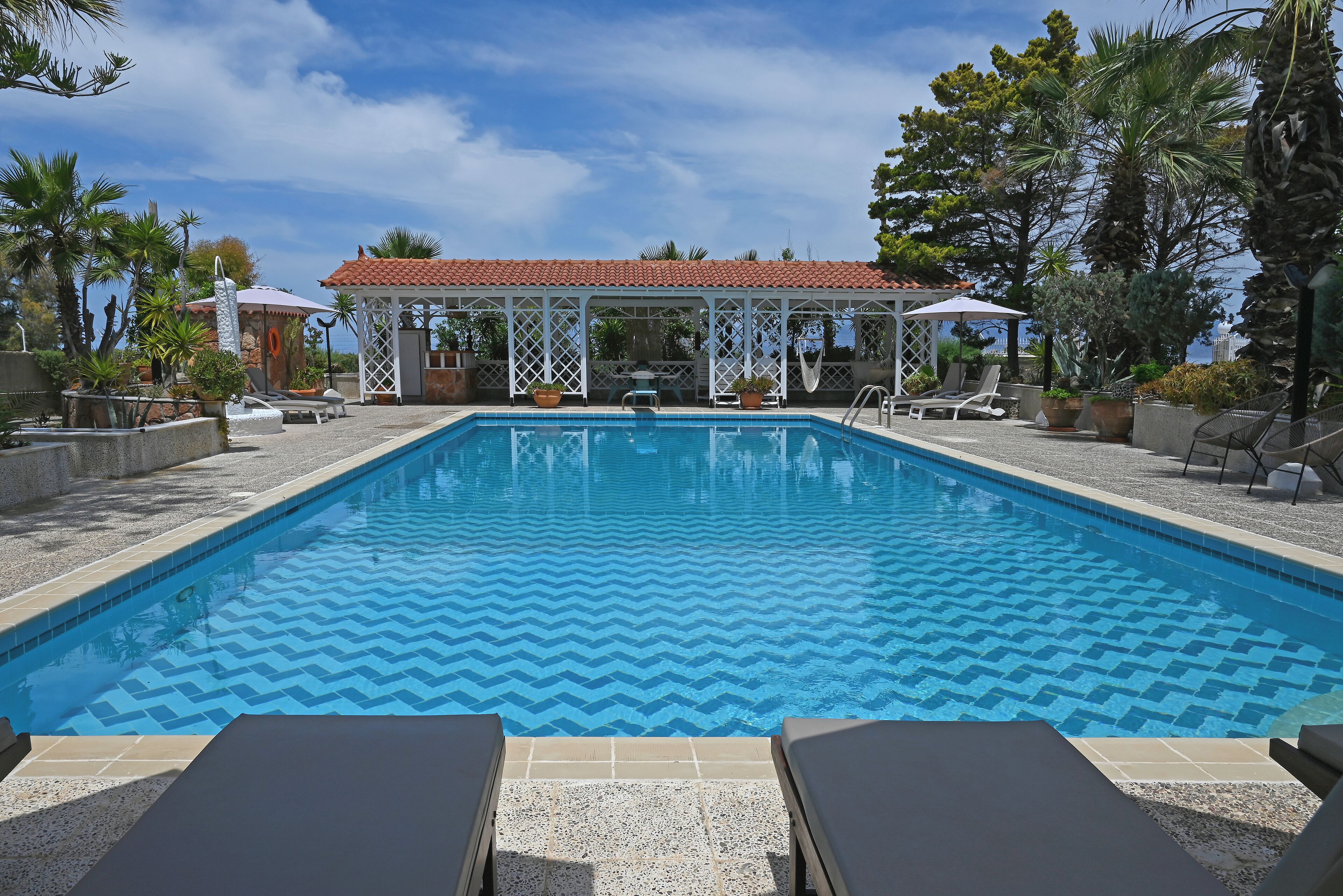 A swimming pool with lounge chairs, a gazebo, and tropical plants.