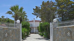 A stone pathway leading to a gated entrance with a white fence and decorative elements. - Villa Supreme (Megara)