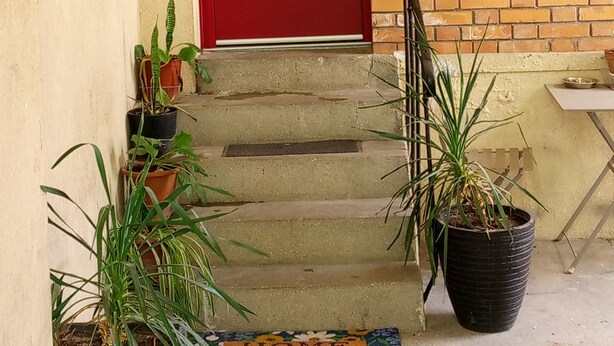A red door with three horizontal handles, a brick wall, and a small outdoor seating area with a table and chairs. - Apartment with garden near Maisons-Alfort veterinary school, metro 8 (Maisons-Alfort)