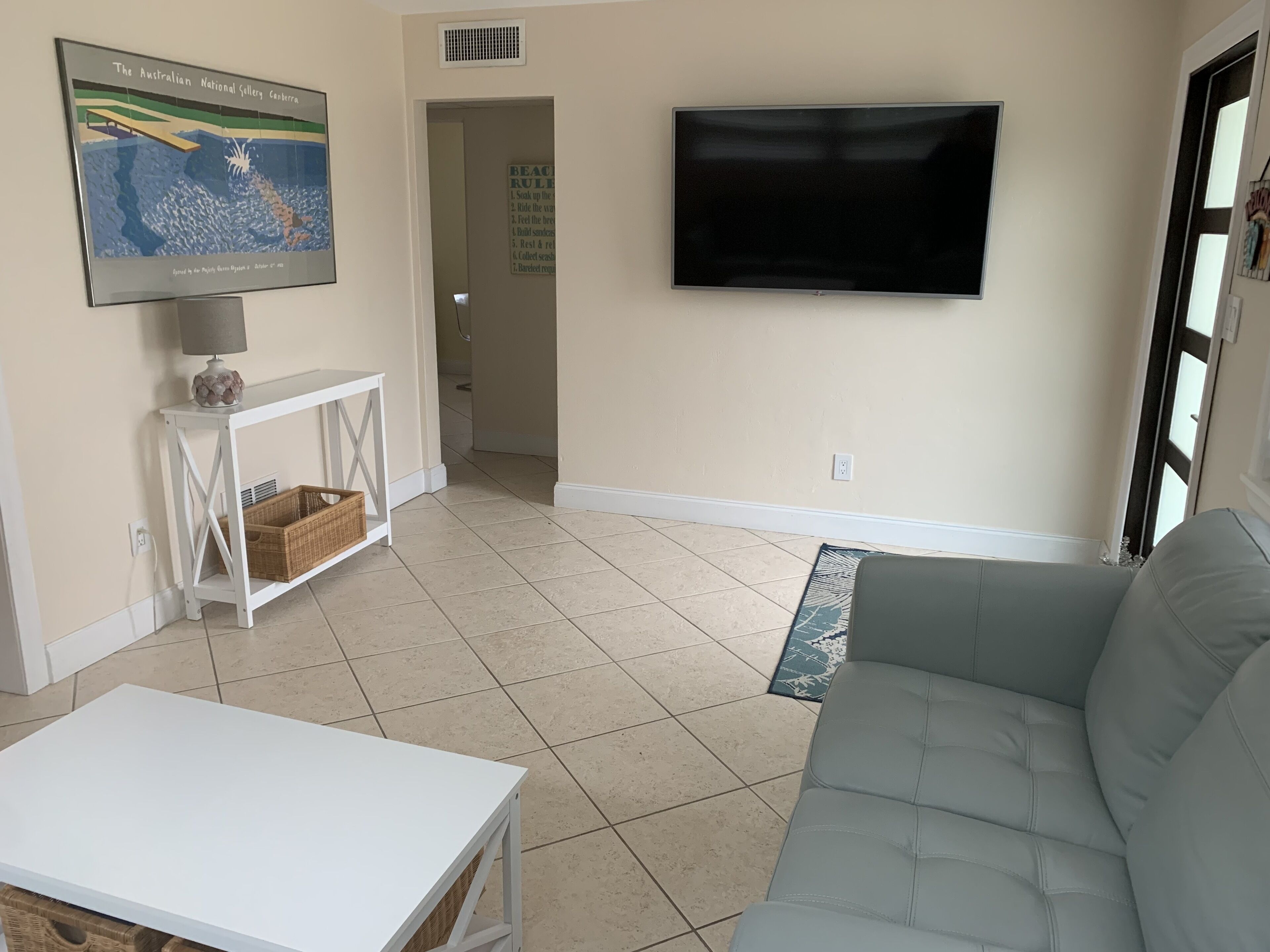 A living room with a white table, grey sofa, and a flat-screen TV mounted on the wall.