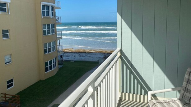 A balcony with a view of the ocean, a building with multiple windows, and a grassy area.