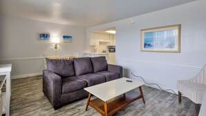 A living room with a gray sofa, a white coffee table, and a kitchen in the background.