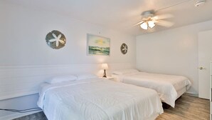 A room with two beds, a ceiling fan, a painting, and a door.