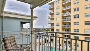 A balcony with a view of a swimming pool, a building with multiple balconies, and a chair.