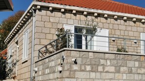 Un edifici de pedra amb teulada vermella, persianes blanques i un balcó amb barana metàl·lica.
