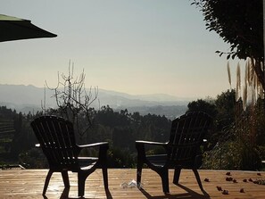 Zwei Stühle auf einer Holzterrasse mit Blick auf Berge und Bäume im Hintergrund.