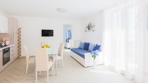 A modern living room with a sofa, a dining table with chairs, a kitchen area with a stove, and a TV mounted on the wall. - SeaView Sorrento Apartment by the sea with terrace  (Sorrento)