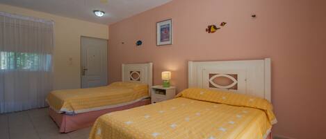 A bedroom with two beds, a ceiling fan, a nightstand with a lamp, and a door.