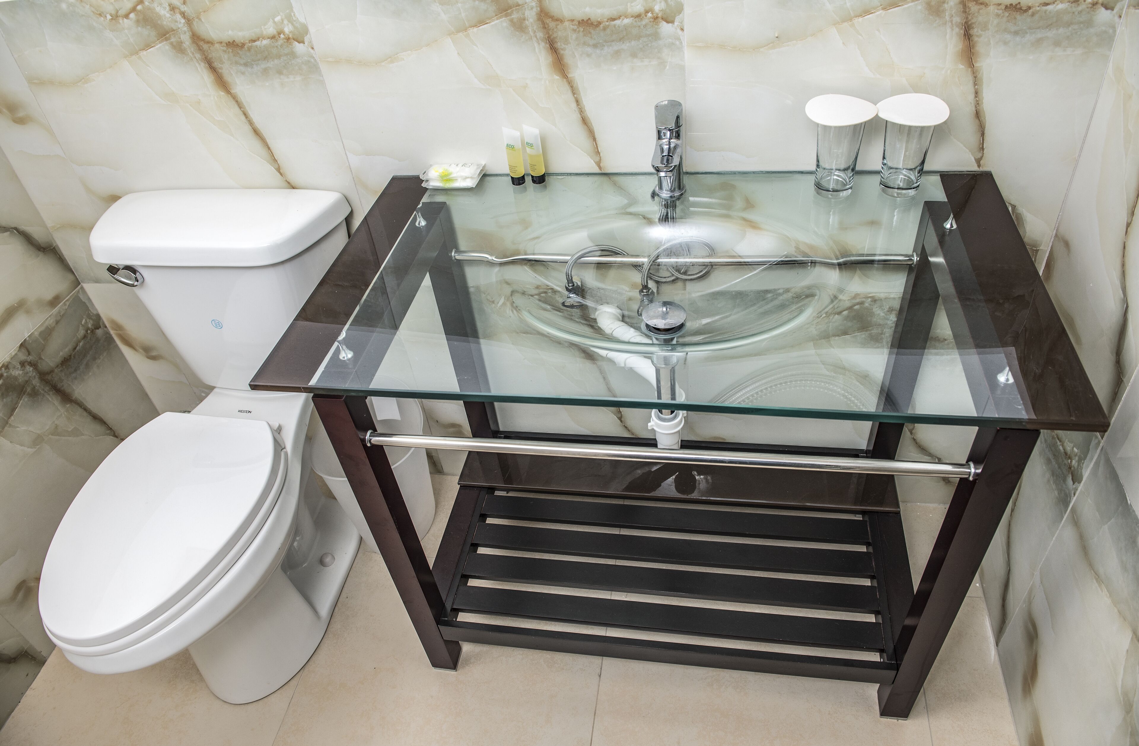 A bathroom with a glass sink, a toilet, and marble walls.