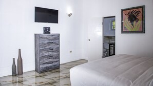 A bedroom with a bed, a TV mounted on the wall, a dresser, and a painting. - Pulse Suites at Villa Ronai (Kingston)