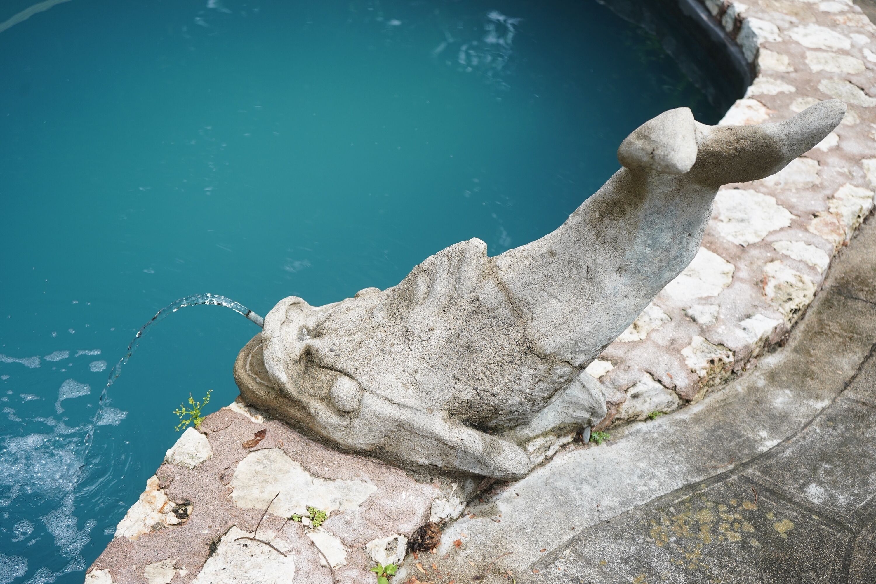 A stone sculpture by a pool with a clear blue water surface.