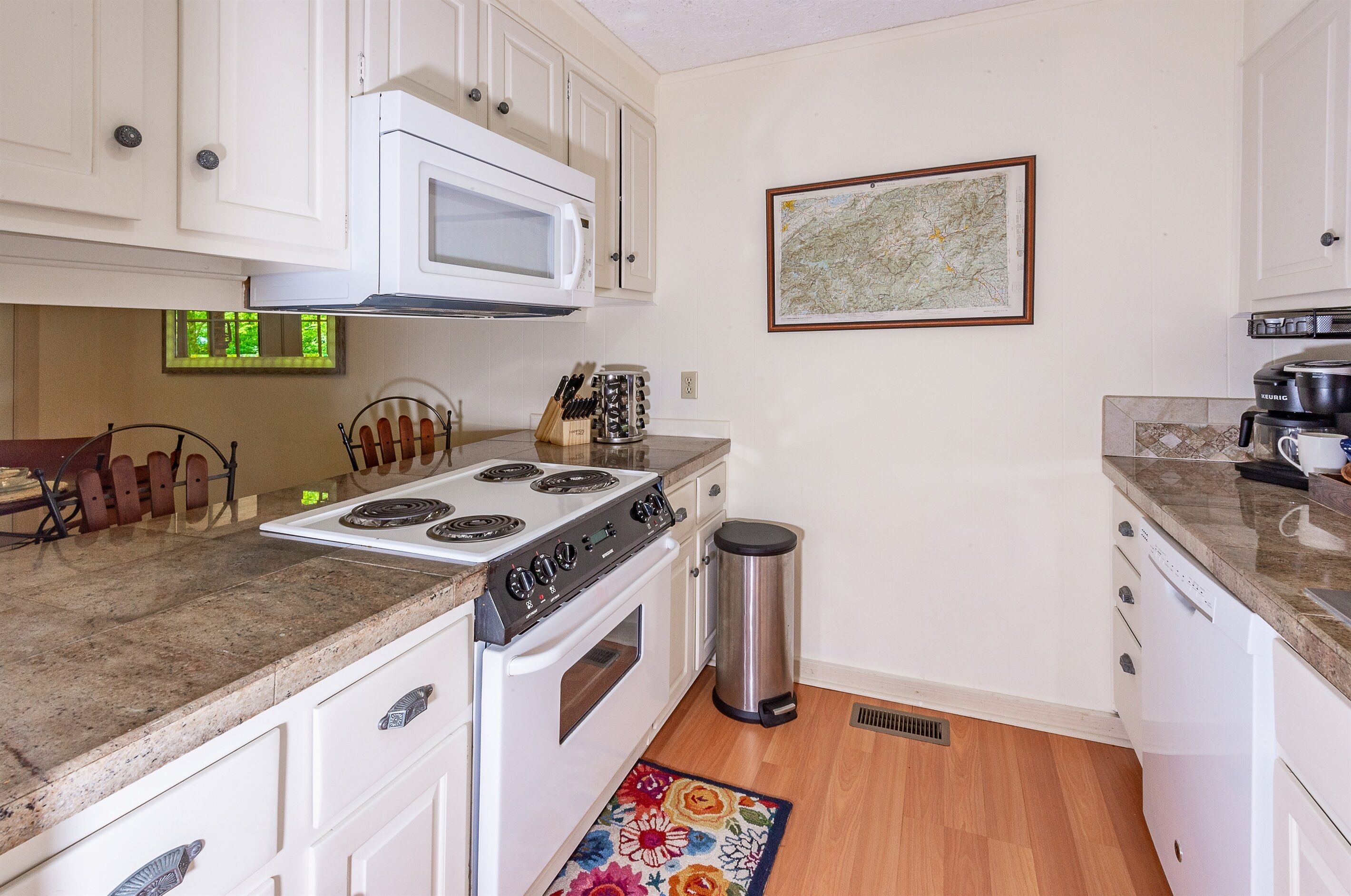 A kitchen with white cabinets, a microwave, a stove, and a trash can.