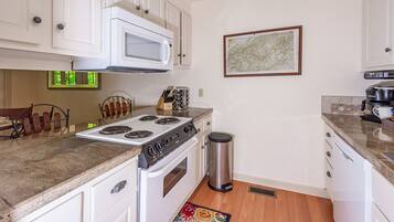 A kitchen with white cabinets, a microwave, a stove, and a trash can.