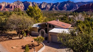 A house with a red roof, surrounded by trees and mountains in the background.