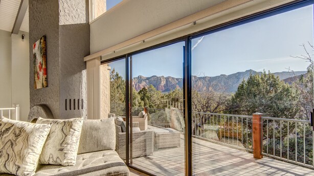 A balcony with a view of mountains, a sofa with patterned cushions, and a painting on the wall.