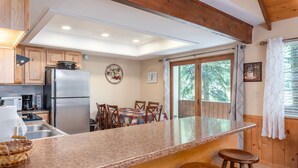 A kitchen with a granite countertop, wooden stools, a stainless steel refrigerator, and a dining table with chairs. - Evergreen B5 (Brian Head)