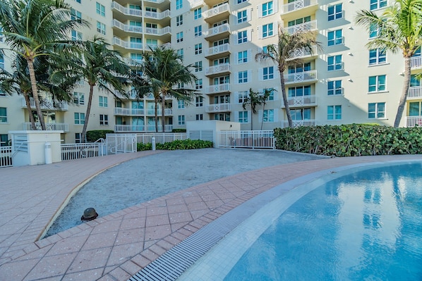 A swimming pool area with a curved edge, surrounded by a brick walkway and palm trees.