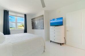 A bedroom with a bed, a dresser, a television, and a window with curtains.