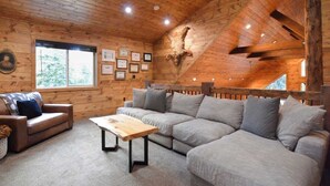 L’intérieur d’une cabane en rondins, avec un canapé, une table basse, des certificats encadrés et une tête d’animal fixée au mur.