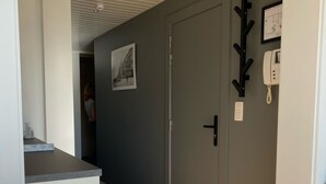 A hallway with a grey door, a coat rack, a wall-mounted phone, and a picture frame. - NICE TWO-BEDROOM APPARTMENT WITH TERRACE (Oostende)