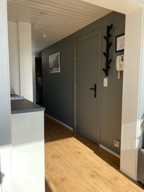 A hallway with a grey door, a coat rack, a wall-mounted phone, and a picture frame.