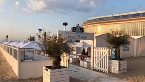 A beach club with a sign reading "BLUE BUDDHA BEACH CLUB WELCOME". There are white structures with umbrellas and seating areas. - NICE TWO-BEDROOM APPARTMENT WITH TERRACE (Oostende)