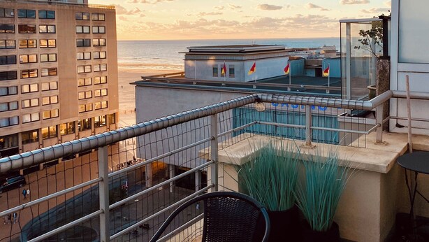 A rooftop terrace with a view of the ocean, featuring a table and chairs, a railing, and potted plants. - NICE TWO-BEDROOM APPARTMENT WITH TERRACE (Oostende)