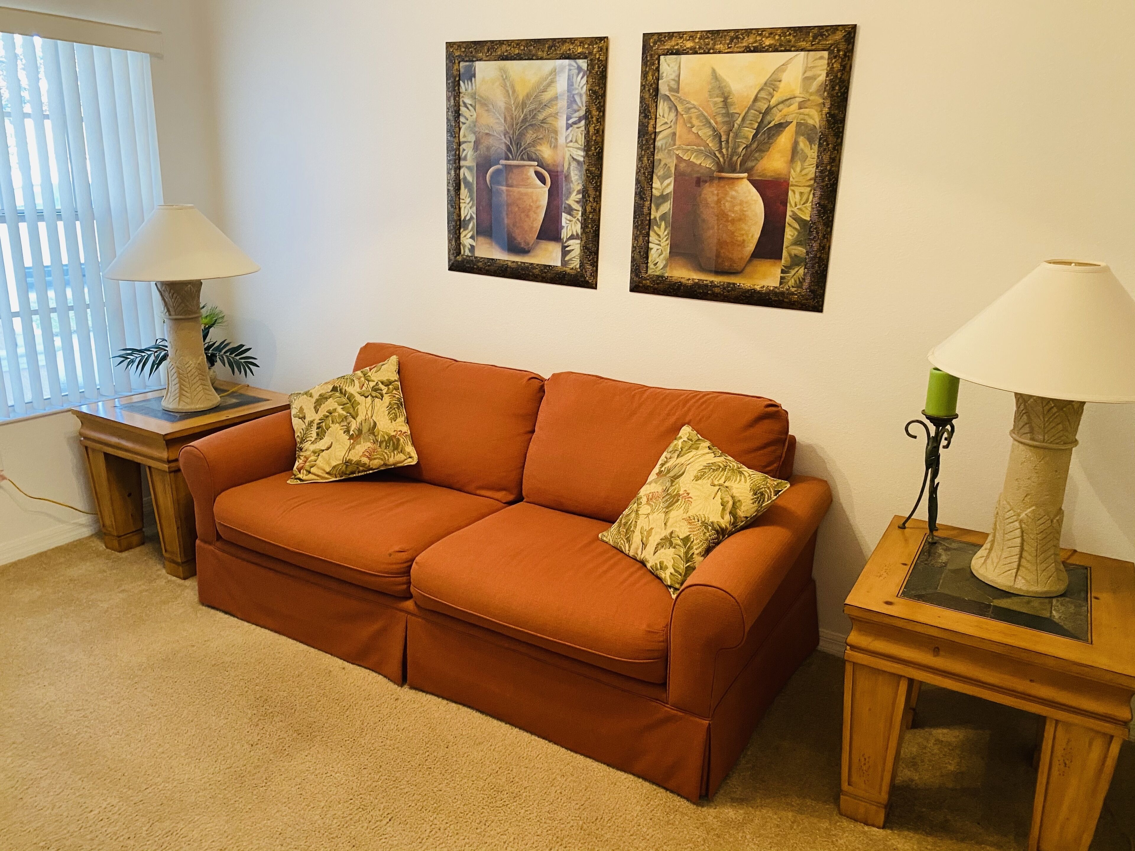 A living room with a sofa, two side tables with lamps, and two framed paintings on the wall.