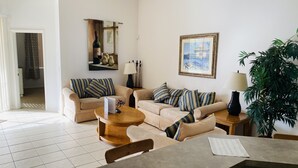 Un soggiorno con due divani beige, un tavolino in legno e un tavolo da pranzo. Si nota anche una pianta in vaso e un quadro appeso al muro.