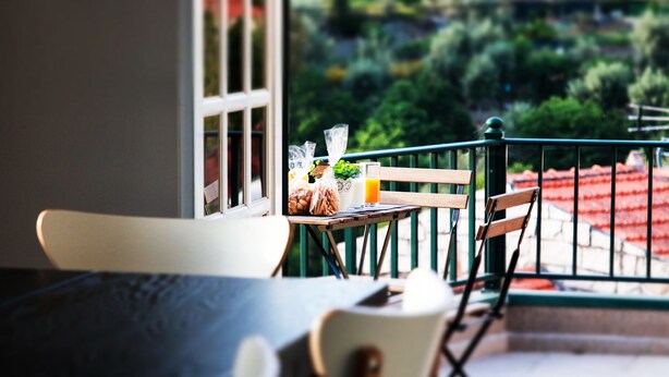 A balcony with a table set for two, a chair, and a view of a red-roofed building and greenery. - Regouro - an Hidden Gem in Douro Valley (Cinfães)