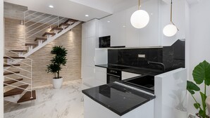 Une cuisine moderne avec un plan de travail en marbre noir, des meubles blancs et un escalier en bois.