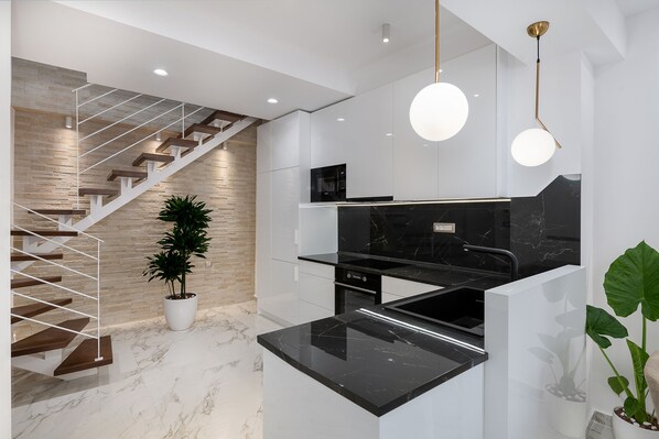 Uma cozinha moderna com bancada de mármore preto, armários brancos e escada de madeira.