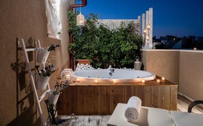 Uma banheira de hidromassagem no terraço, com um deck de madeira, rodeada por vasos de plantas e velas.
