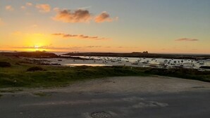 A coastal road with a sunset view, a grassy area, and a marina with boats. - LA GABARDISE (Plouarzel)