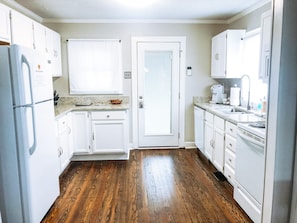Una cocina con armarios blancos, piso de madera, refrigerador, estufa y pileta.