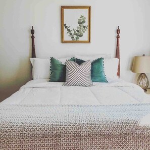 Una cama con un edredón blanco, dos almohadas e impresión enmarcadas de motivos botánicos arriba.