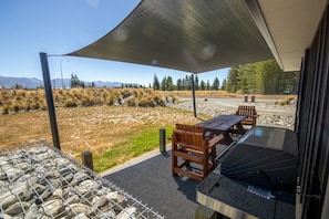 An outdoor patio with a barbecue grill, wooden tables, and chairs.