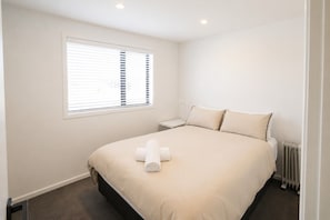 A bedroom with a bed, a nightstand, a window with blinds, and a radiator. - Tussock Treasure - Exclusive Use (Twizel)