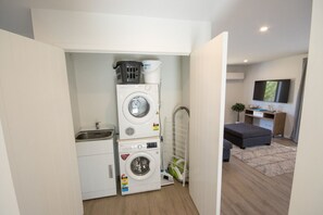 A compact laundry room with stacked washing machines, a drying rack, and a small sink.