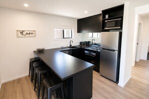 A modern kitchen with a central island, black cabinetry, stainless steel appliances, and a 'Love' sign on the wall. - Tussock Treasure - Exclusive Use (Twizel)