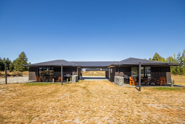 A modern outdoor structure with two covered areas, each featuring a barbecue grill and seating.