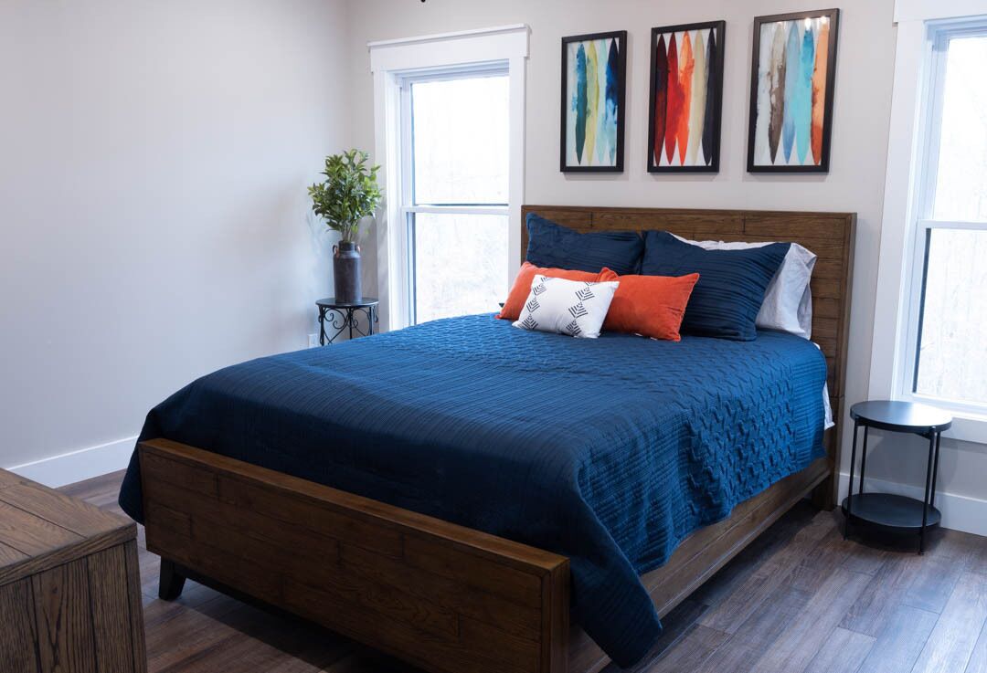 Een slaapkamer met een houten bed, blauw beddengoed en drie ingelijste kunstwerken aan de muur.